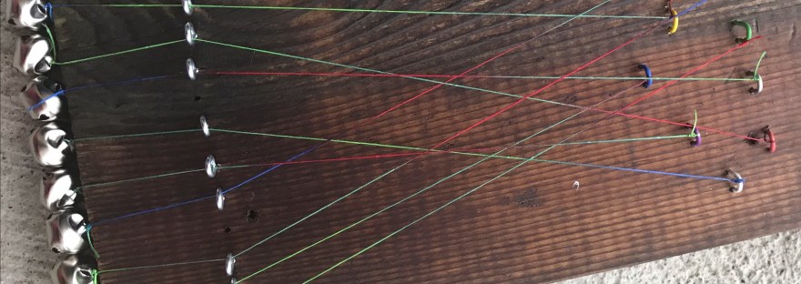 Photograph of a wooden board with strings and bells attached.